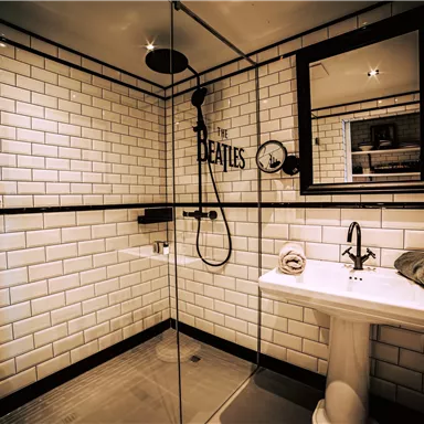 A modern bathroom with white brick walls and a glass shower. The room features a sink and decorative elements with the inscription "THE BEATLES".