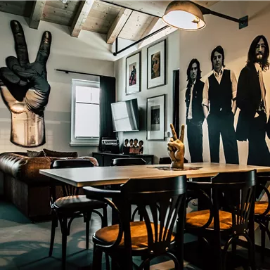 A modern living room with a large sofa and a dining table. On the wall, there are stylized pictures of people and a large hand displaying the peace sign.