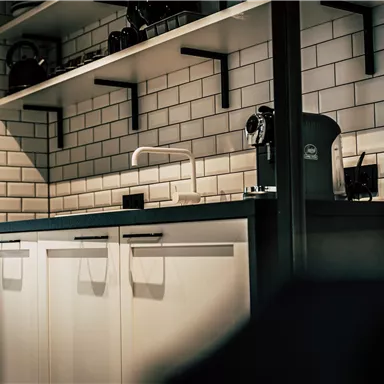 A modern kitchen with white cabinets and an elegant countertop. On the shelves, various kitchen utensils and a coffee machine can be seen.