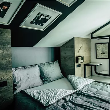 A modern bedroom with a cozy bed and stylish wood paneling. Above the bed hang picture frames, and there is a minimalist coat rack.