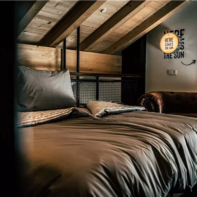 A cozy bedroom with wooden beams and a large bed. A lamp with an inspiring quote hangs on the wall.