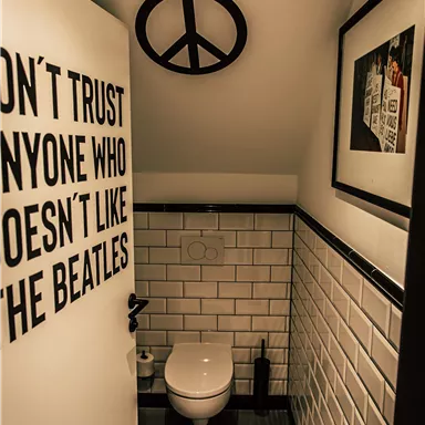 A modern bathroom with white tiles and a minimalist look. On the wall hangs a sign with a message about the Beatles.