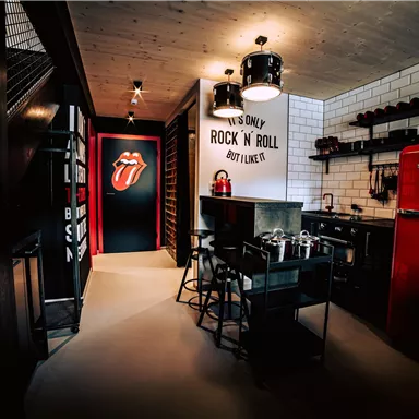 A modern kitchen with a red refrigerator and stylish furniture. The walls are decorated with Rock'n'Roll themes.