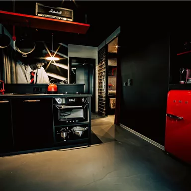 A modern kitchen with black cabinets and a red refrigerator. The atmosphere is stylish and well-designed.