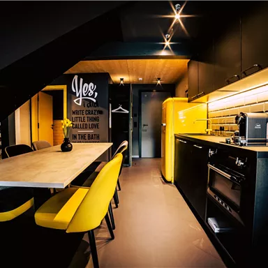 A modern kitchen with a yellow refrigerator and black furnishings. Yellow chairs are at the table, which lighten up the room.