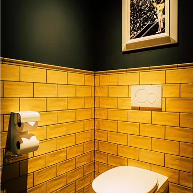 A modern bathroom with yellow tiles and a spacious toilet. A black and white photo hangs on the wall.