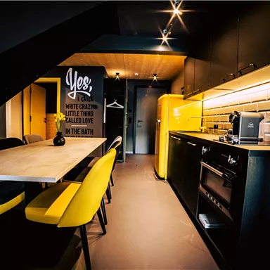A modern kitchen with black furniture and yellow chairs. The walls are decorated with decorative tiles and an inspiring quote.