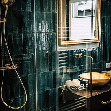 A modern bathroom with a rain shower and an elegant sink. The space features green tiles and a large mirror.