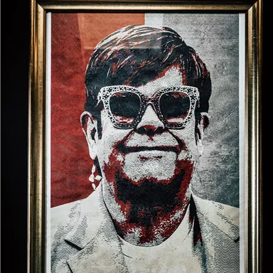 An artistic portrait of a person wearing sunglasses and with a cheerful expression. The background is designed in shades of red.