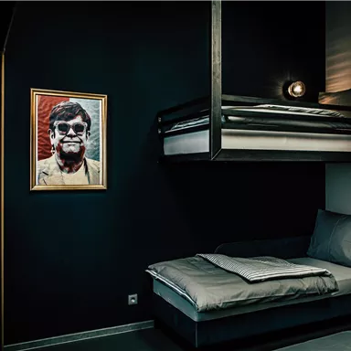 A modern room with a bunk bed and a single bed. A painted portrait in a golden frame hangs on the wall.