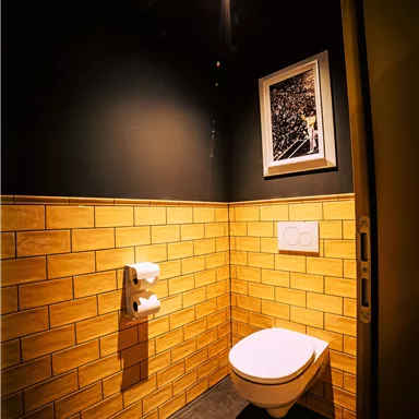 A modern bathroom with yellow tiles and dark wall color. A stylish toilet stands in the foreground, illuminated by a ceiling spotlight.