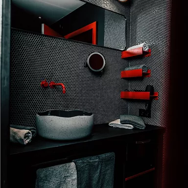 A modern bathroom with a large sink and elegant black walls. Red accents give the space a stylish touch.