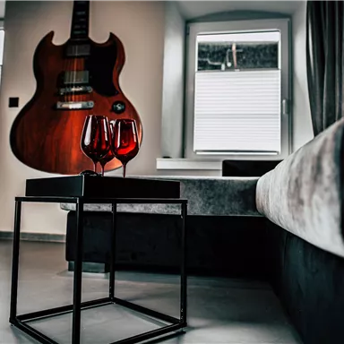 A modern living room with an acoustic guitar on the wall. On a table, there are two filled wine glasses.