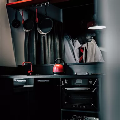 A modern kitchen with black design and red accents. On the countertop, there are pots and a red tea or coffee pot.