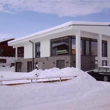 A modern house in the midst of a snowy landscape. The surroundings are quiet with snow-covered trees and a clear winter sky.