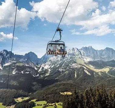 A cable car glides over green meadows and majestic mountains. The sky is clear and the landscape is stunning.