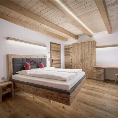Ein modernes Schlafzimmer mit Holzdekor und einem großen Bett. Der Raum ist hell und freundlich mit einem Schreibtisch und einem Schrank.