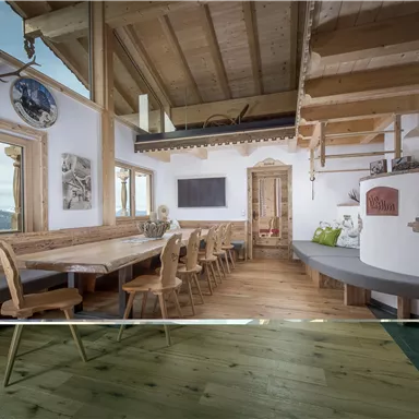 Ein gemütlicher Raum mit Holzinterieur und einem großen Esstisch. Im Hintergrund sind Berglandschaften durch die Fenster sichtbar.