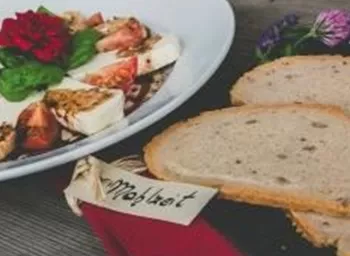 A delicious salad with tomatoes, mozzarella, and fresh basil leaves on a white plate. Next to it are two slices of bread on a wooden board.