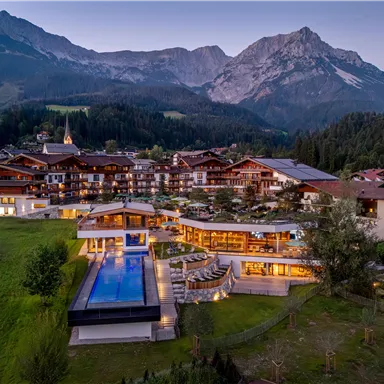 Ein malerisches Hotel in den Bergen mit einer modernen Architektur und einem schönen Pool. Die Umgebung besteht aus grünen Wiesen und majestätischen Bergen.