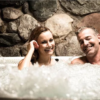 A couple relaxes in a hot tub. They are smiling and enjoying their time together.