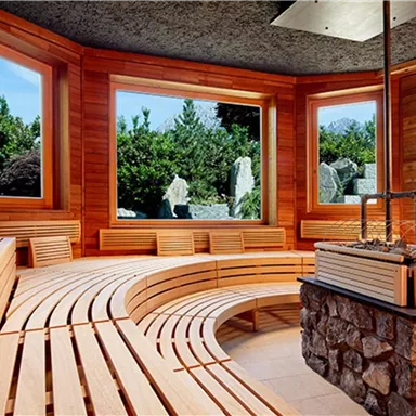 A bright sauna with wooden benches and large windows. Outside, you can see lush greenery and rocks.