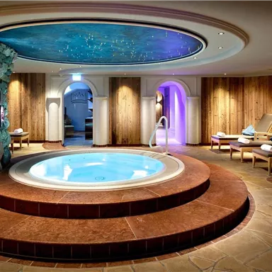 An elegant spa area with a round whirlpool and a glittering starry sky. Relaxing loungers and warm wood paneling create a tranquil atmosphere.