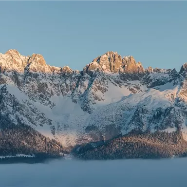 An impressive mountain landscape with snow-covered peaks. The sky is clear and the light of the morning sun illuminates the mountains.