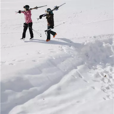 Two children are walking in the snow and wearing skis. They are pointing in different directions with their hands.