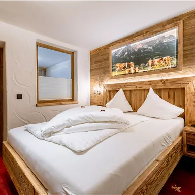 A cozy bedroom with a wooden bed and white pillows. A landscape picture hangs on the wall, and the floor is covered with a red carpet.