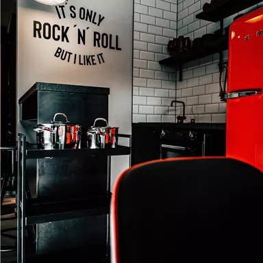 A modern kitchen with a red refrigerator and a stylish shelf.  
On the wall is the saying "It's only rock 'n' roll, but I like it."