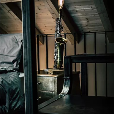 A stylish bedroom with a bed and a nightstand.  
On the nightstand, there is a decorative saxophone lamp.