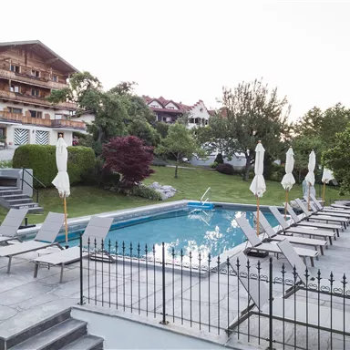 A beautiful outdoor area with a pool and loungers. The surroundings are green and well-maintained, perfect for relaxing.