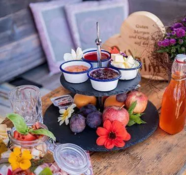 A lovingly arranged dessert plate with various sauces, fresh fruits, and blooming decorations. Next to it is a bottle of juice and a prettily designed wooden figure.