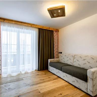 A cozy room with a bright sofa and a television. Large windows provide plenty of daylight and a view outside.