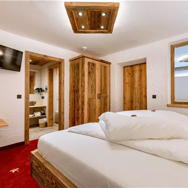 A modern bedroom with a large bed and wooden furniture. The room has a television and a pleasant atmosphere.
