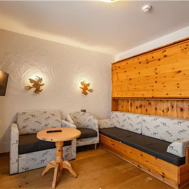 A cozy room with a wooden bench and a round table. The walls are designed with bright colors and decorative elements.