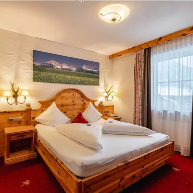 A cozy bedroom with a wooden bed and red carpet. The room is bright and invites relaxation.
