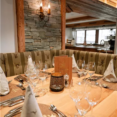 An elegant table in a cozy restaurant with glasses, cutlery, and decorative napkins. The walls are made of stone and wood, creating a warm atmosphere.