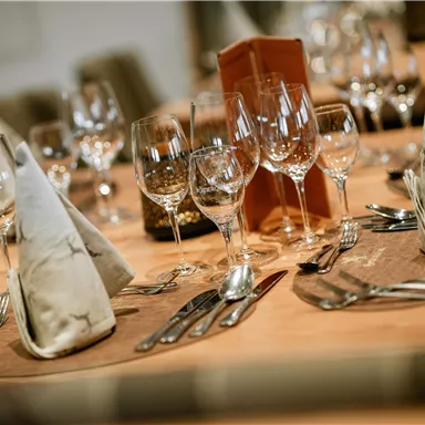 An elegantly set table with cutlery, glasses, and decorated napkins. The warm wood look creates an inviting atmosphere.