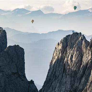 Nowadays, you see balloons above an impressive mountain landscape. The rugged peaks stand out against a soft, misty background.