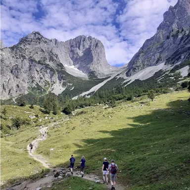 A picturesque mountain landscape with high peaks and a green meadow. Hikers are walking on a path through nature.