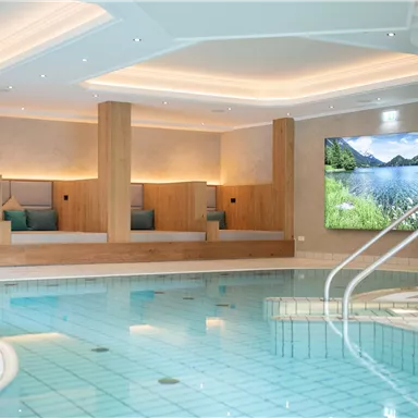 An elegant wellness area with an indoor pool and comfortable loungers for relaxing. On the wall, there is a large picture of a picturesque landscape.