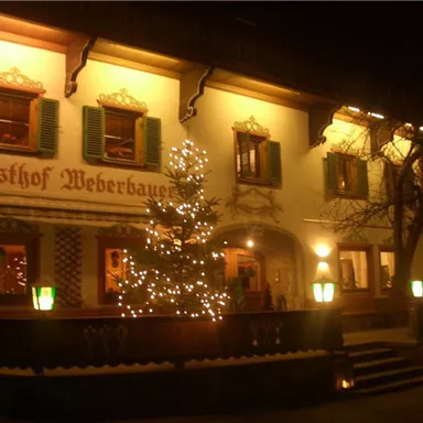 A traditional inn with a festively decorated Christmas tree. The facade is illuminated and invites guests.