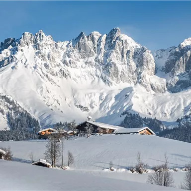 A snowy landscape with majestic mountains in the background. In the foreground, some cottages and trees are visible.
