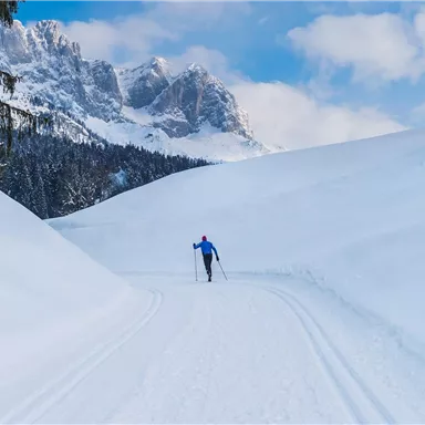 A skier is running on a snowy track. In the background, majestic mountains and a blue sky can be seen.