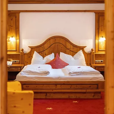 A cozy bedroom with a wood-accented bed and white pillows. The floor is red with a star pattern, and a yellow sofa is in the foreground.