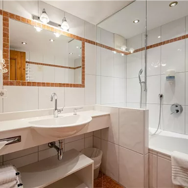 A modern bathroom with a shower and a bathtub. The white tiles and the good lighting create a bright atmosphere.