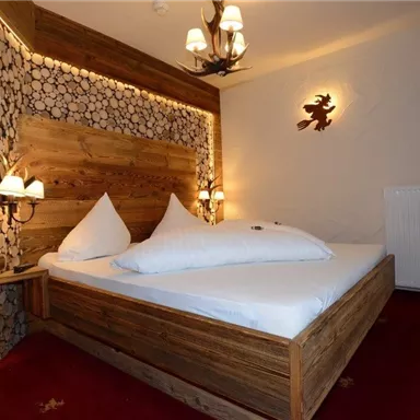 A cozy bedroom with a wooden bed and decorative pillows. The warm light accents and the wooden paneling create an inviting atmosphere.