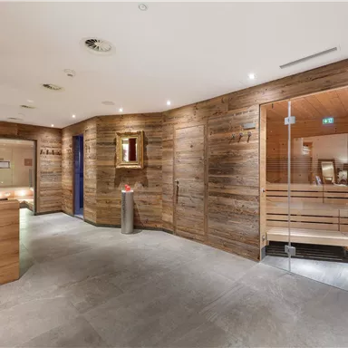 A modern-designed wellness area with wooden-paneled walls. On display are a glass sauna and a reception area.